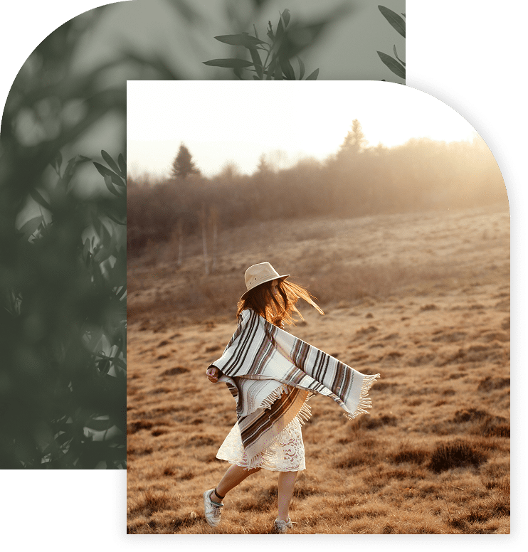 Woman in a hat and shawl joyfully spinning in an open field at sunset.