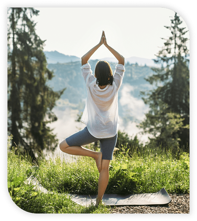 Yoga pose in the grass surrounded by trees and mountains.