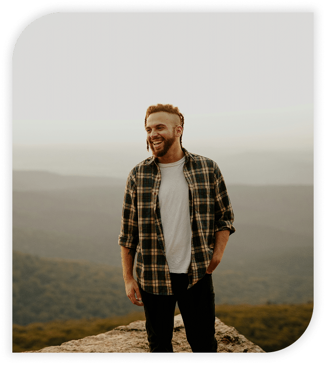Smiling man standing on a mountain overlook at sunset.