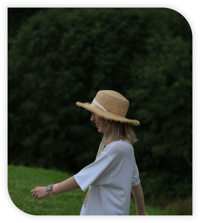 Woman in a straw hat smiling and walking in a grassy field.