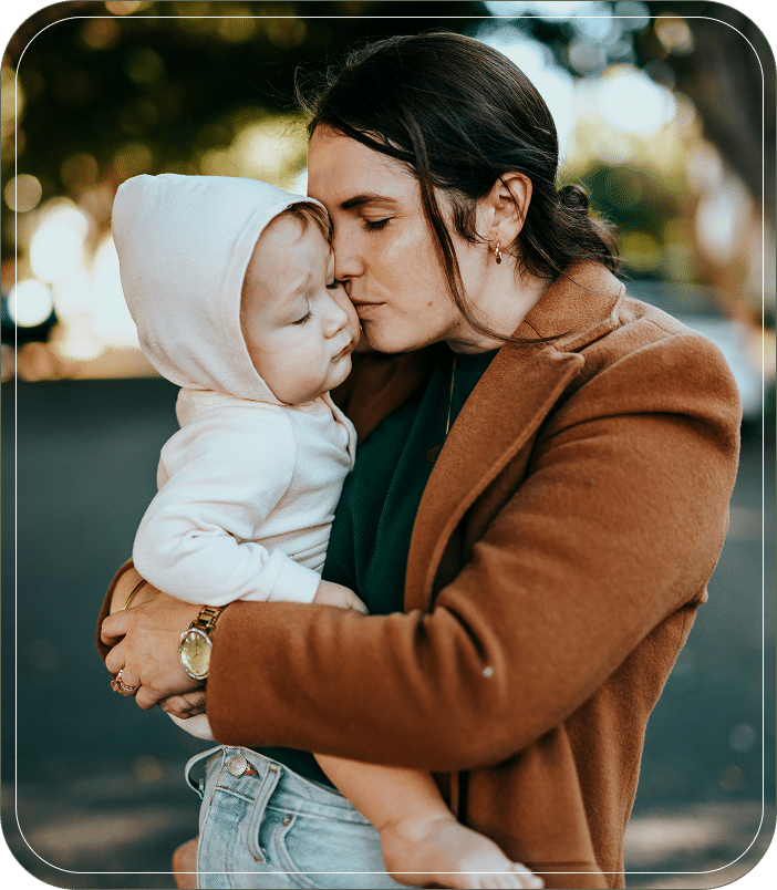 Mother holding and kissing her baby outdoors, both dressed warmly.