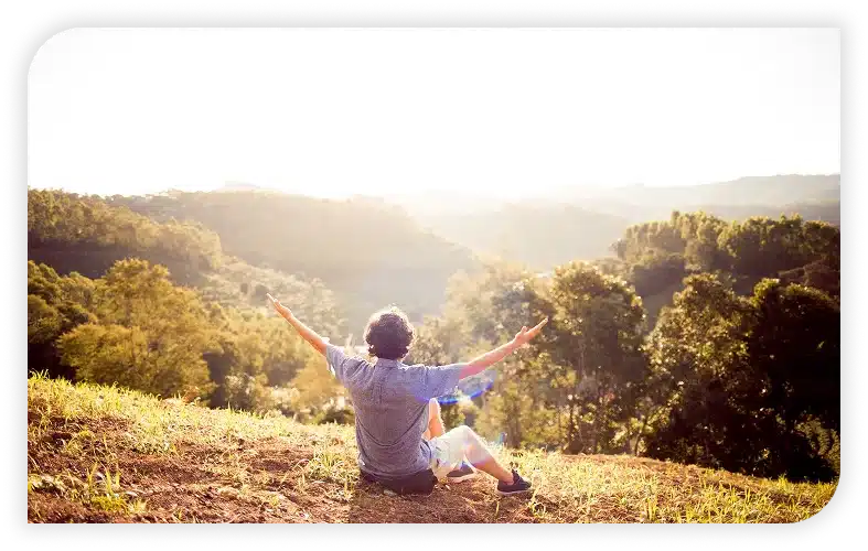 A person sits on a hillside with arms outstretched.