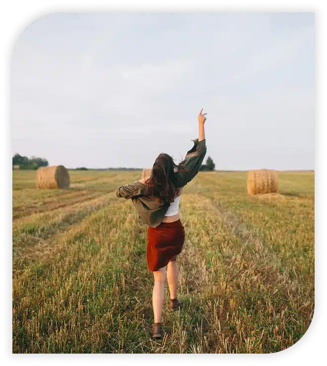 A young woman running through a field with hay bales.